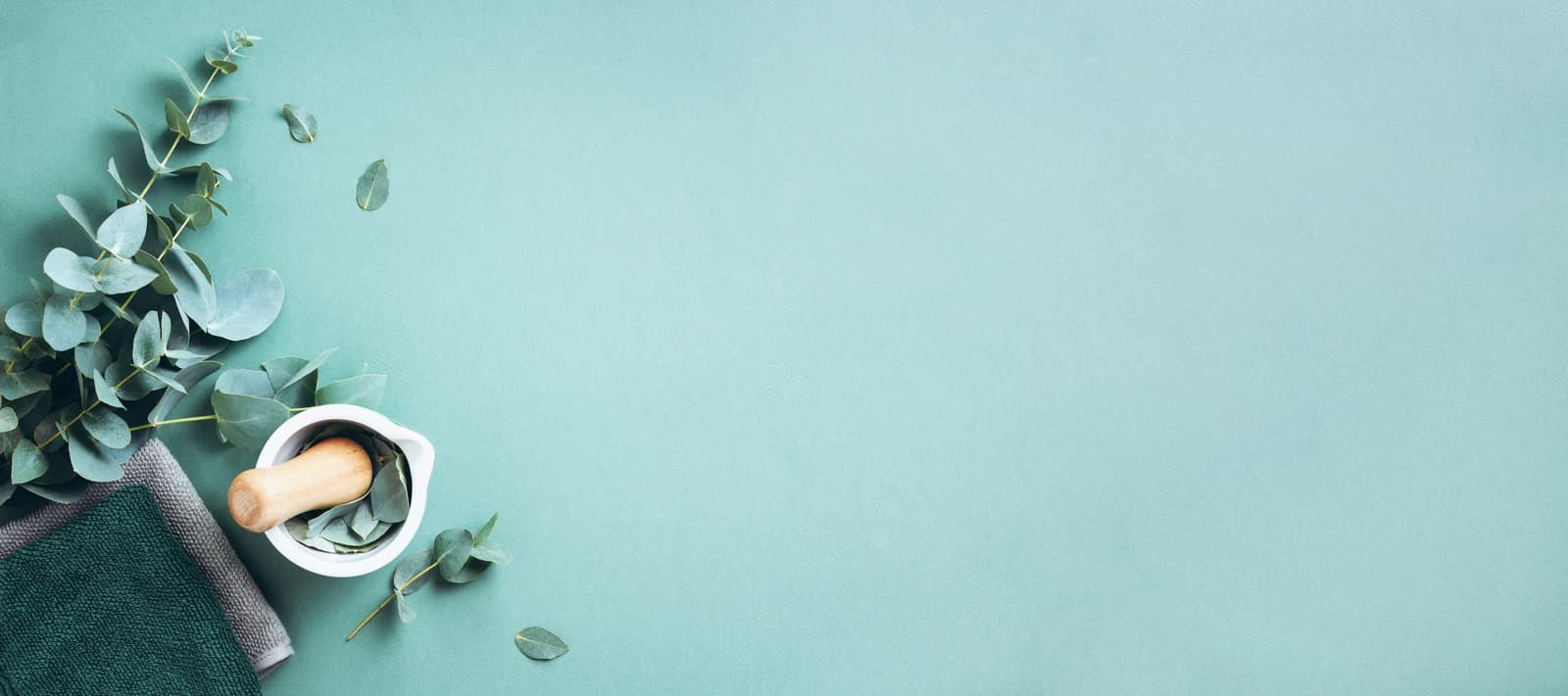 Eucalyptus, mortar and spa towels on a soft teal background